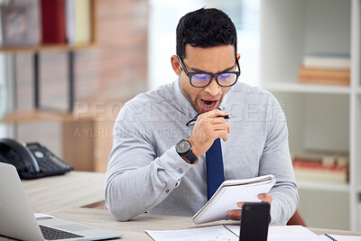 Buy stock photo Young tired mixed race businessman reading notes In a notebook alone in an office at work. One hispanic male businessperson yawning while writing in a diary sitting at a desk in an office