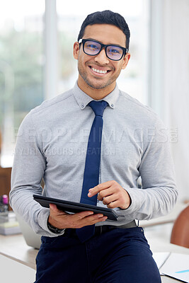Buy stock photo Young mixed race businessman holding and using a digital tablet standing in an office at work. One content hispanic male businessperson typing on a digital tablet at work