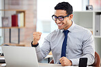 Young happy mixed race businessman cheering with his fist in joy while working on a laptop at work. Cheerful hispanic male businessperson celebrating success and victory in an office