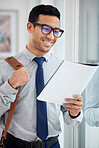 Content mixed race businessman reading a report alone in an office at work. Hispanic male businessperson wearing glasses looking at a document while standing in an office