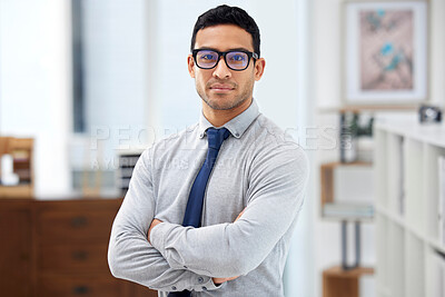 Buy stock photo Young serious mixed race businessman standing with his arms crossed alone in an office at work. Headshot of a confident hispanic businessperson wearing glasses while standing at work