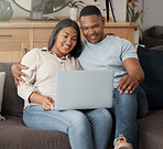 Attractive young mixed race couple relaxing on the sofa and using a laptop. Smiling African American couple watching movies while being affectionate and bonding at home together