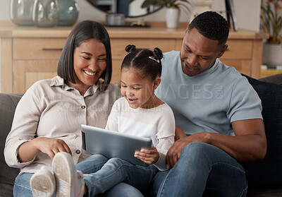 A happy mixed race family of three relaxing on the sofa at home. Loving black family being affectionate on the sofa while using a digital tablet and streaming. Young couple bonding with their daughter and watching movies at home