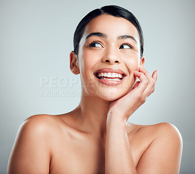 A beautiful young mixed race woman with glowing skin posing against grey copyspace background. Hispanic woman with natural looking eyelash extensions smiling while feeling her smooth skin in a studio