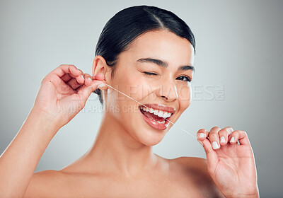 Studio portrait of a smiling mixed race young woman with glowing skin posing against grey copyspace background while flossing her teeth for fresh breath. Hispanic model using floss to prevent a cavity