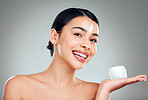 Studio Portrait of a beautiful smiling mixed race woman applying cream to her face. Hispanic model with glowing skin holding moisturiser against a grey copyspace background