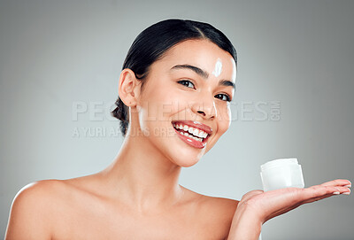 Buy stock photo Studio Portrait of a beautiful smiling mixed race woman applying cream to her face. Hispanic model with glowing skin holding moisturiser against a grey copyspace background