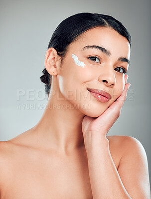 Buy stock photo Studio Portrait of a beautiful smiling mixed race woman applying cream to her face. Hispanic model with glowing skin grey copyspace background
