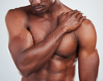 Buy stock photo One unknown muscular fitness model experiencing shoulder pain from an injury while exercising. Black topless athlete holding his arm in pain while isolated on grey copyspace in a studio