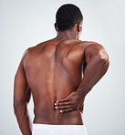 One unknown muscular fitness model experiencing back pain from poor posture while exercising. Black topless athlete with backache while isolated on grey copyspace in a studio