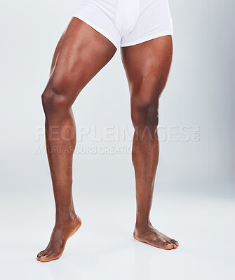 Closeup of one African American fitness model posing in a underwear and looking muscular. Confident black male athlete isolated on grey copyspace in a studio wearing boxers with strong, toned legs