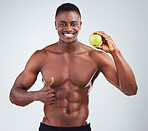 Portrait of a smiling African American fitness model posing topless with an apple and looking muscular. Happy black male athlete isolated on grey copyspace showing the thumbs up to a healthy diet
