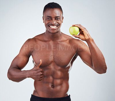 Buy stock photo Portrait of a smiling African American fitness model posing topless with an apple and looking muscular. Happy black male athlete isolated on grey copyspace showing the thumbs up to a healthy diet