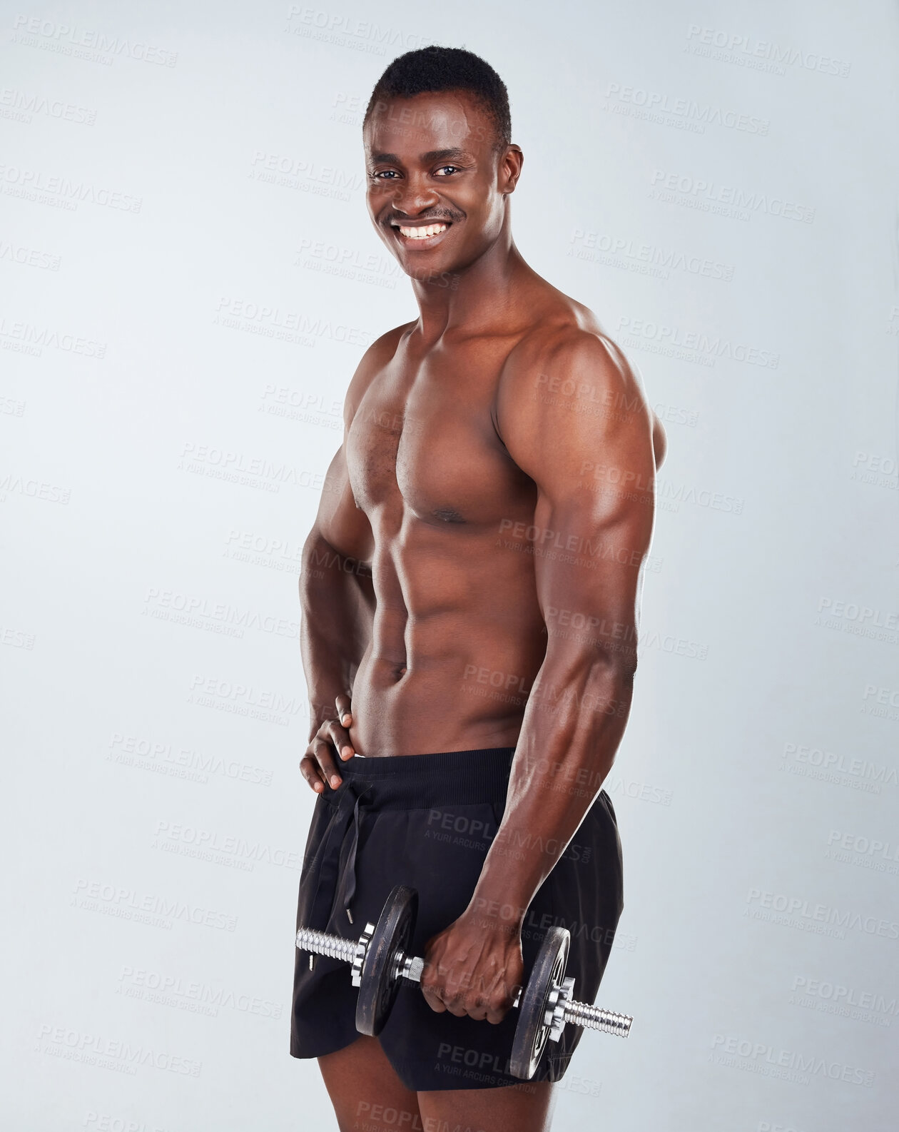 Buy stock photo Portrait of a smiling African American fitness model posing topless while exercising with dumbbells .Happy black male athlete isolated on grey copyspace while weightlifting in a studio