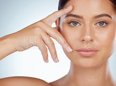 Closeup of beautiful woman with smooth glowing skin touching face in studio. Headshot of serious caucasian model isolated against grey background and showing manicured hand. Healthy self care routine