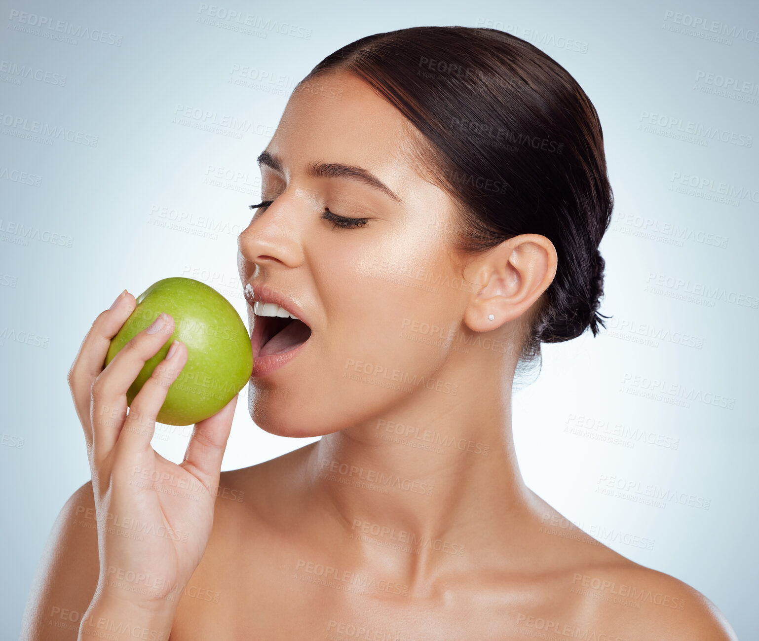 Buy stock photo Beautiful woman biting into a green apple while posing with copyspace. Caucasian model isolated against a grey background in a studio. Eating healthy and dieting is part of a good skincare routine