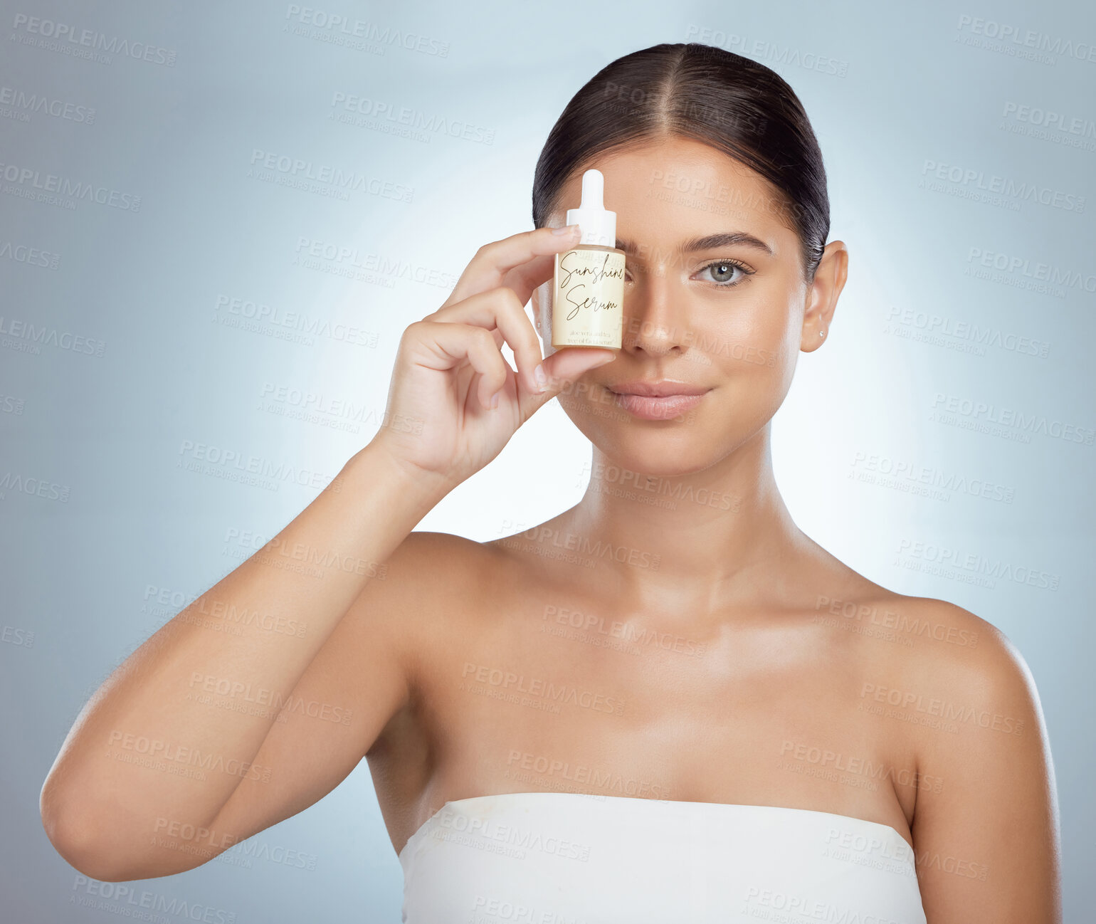 Buy stock photo Portrait of beautiful woman holding face serum over eye while posing with copyspace. Young caucasian model isolated against grey studio background. Using skin oil for healthy glowing skincare routine