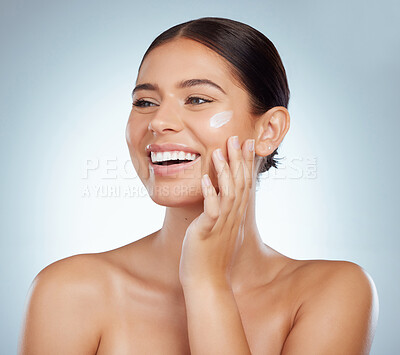 Buy stock photo Smiling beautiful woman applying face cream while posing with copyspace. Caucasian model isolated against grey studio background with product on cheek. Moisturise and sunscreen for healthy skincare