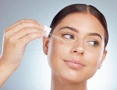 Closeup of a beautiful woman using dropper to apply face serum to her cheek. Caucasian model isolated against a grey background in a studio using skin oil for healthy glowing skin in skincare routine