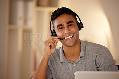 One young man wearing headset and working on a laptop in an office at night. Happy guy doing freelance work as a call centre agent. Consultant operating a helpdesk for customer care, sales and support