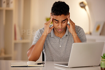 Young stressed man working alone on a laptop in an office at night. Guy looking tired and worried while struggling with burnout and a headache from problems, deadlines and pressure at work