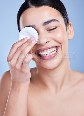 A beautiful smiling mixed race woman using a cotton pad to remove makeup during a selfcare grooming routine. Hispanic woman applying cleanser to her face against blue copyspace background