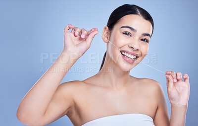 Studio portrait of a smiling mixed race young woman with glowing skin posing against blue copyspace background while flossing her teeth for fresh breath. Hispanic model using floss to prevent a cavity