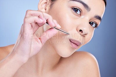 Buy stock photo Studio portrait of a beautiful  mixed race young woman with glowing skin posing against blue copyspace background while tweezing her lip. Hispanic model using a tweezer for hair removal