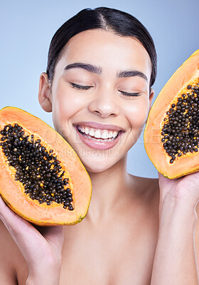 A happy smiling mixed race woman holding a papaya. Hispanic model promoting the skin benefits of a healthy diet against a blue copyspace background