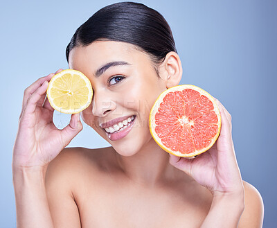 Buy stock photo Portrait of a happy mixed race woman holding a lemon and grapefruit. Hispanic model promoting the skin benefits of citrus against a blue copyspace background