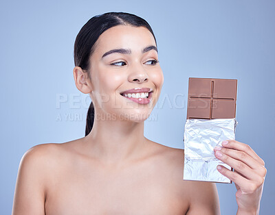Buy stock photo A beautiful mixed race woman holding a slab of chocolate. Hispanic model snacking on dessert against a blue copyspace background