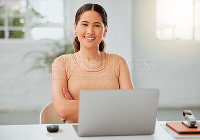 Portrait of one confident young hispanic business woman working on a laptop in an office. Happy entrepreneur browsing the internet while planning ideas at her desk in a creative startup agency