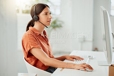 One young hispanic female call centre telemarketing agent talking on a headset while working on a computer in an office. Focused mixed race business woman consultant operating helpdesk for customer service support