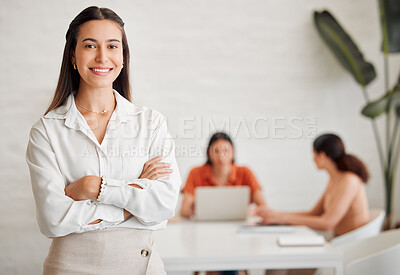Portrait of one confident young hispanic business woman standing with arms crossed in an office with her colleagues in the background. Ambitious entrepreneur and determined leader ready for success in a creative startup agency