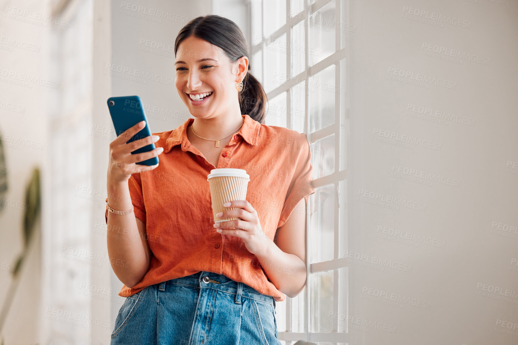 Buy stock photo Young happy mixed race businesswoman using her phone while drinking a coffee alone in an office at work. One cheerful hispanic businessperson using social media on her cellphone while holding a coffee cup on a break while standing at work