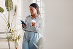 African american businesswoman using her phone while drinking a coffee alone in an office at work. One black female businessperson using social media on her cellphone and holding a coffee cup on a break standing at work