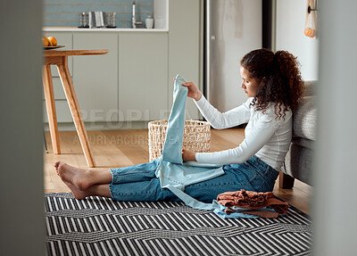 Young woman sitting on the floor folding laundry. Woman folding fresh,cleaned laundry at home. Woman cleaning her clothing and bedding. Woman busy with housework chores.