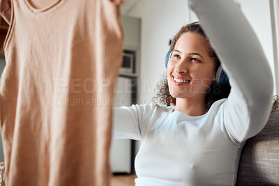 Buy stock photo Woman listening to music in headphones. Young woman looking at fresh, cleaned laundry. Happy woman holding washed top. Young woman enjoying music and housework chores. Woman cleaning her clothing