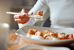 Closeup of woman eating plate of sushi with chopsticks. Hand of a woman enjoying a meal at home. Woman enjoying asian food at home. Delicious sushi is always a great meal. Woman eating seafood