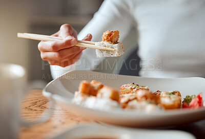 Buy stock photo Closeup of woman eating plate of sushi with chopsticks. Hand of a woman enjoying a meal at home. Woman enjoying asian food at home. Delicious sushi is always a great meal. Woman eating seafood