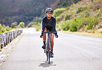 One athletic young woman cycling outside. Sporty fit female wearing helmet and glasses while riding a bike on a road along the mountain for exercise. Endurance and cardio during a workout and training