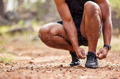Closeup of an athlete tying his shoelaces before going for a run outside. Athletic man getting ready for training outdoors in nature. Muscular runner about to do some warmup exercises before cardio.
