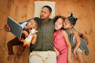A happy mixed race family of four relaxing and lying on the lounge floor together. Loving black single parent bonding with his kids while using a digital tablet to take a selfie
