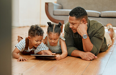 A happy mixed race family of three relaxing and lying on the lounge floor together. Loving black single parent bonding with his kids while using a digital tablet stream