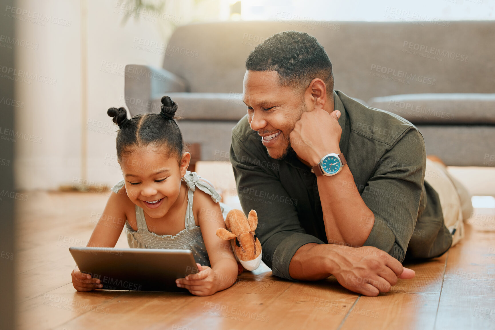 Buy stock photo A happy mixed race family of two relaxing and lying on the lounge floor together. Loving black single parent bonding with his daughter while using a digital tablet to watch movies