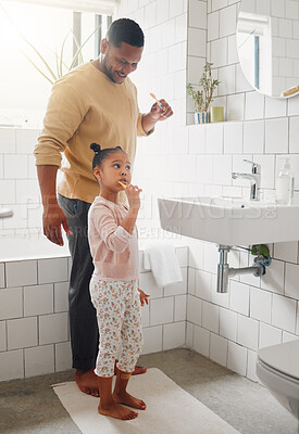 Buy stock photo Happy mixed race father and daughter brushing their teeth together in a bathroom at home. Single African American parent teaching his daughter to protect her teeth