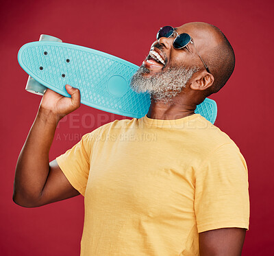 One mature african american man standing with a mini skateboard in studio isolated against a red background. Handsome and carefree man wearing sunglasses and laughing happily. He is ready for summer
