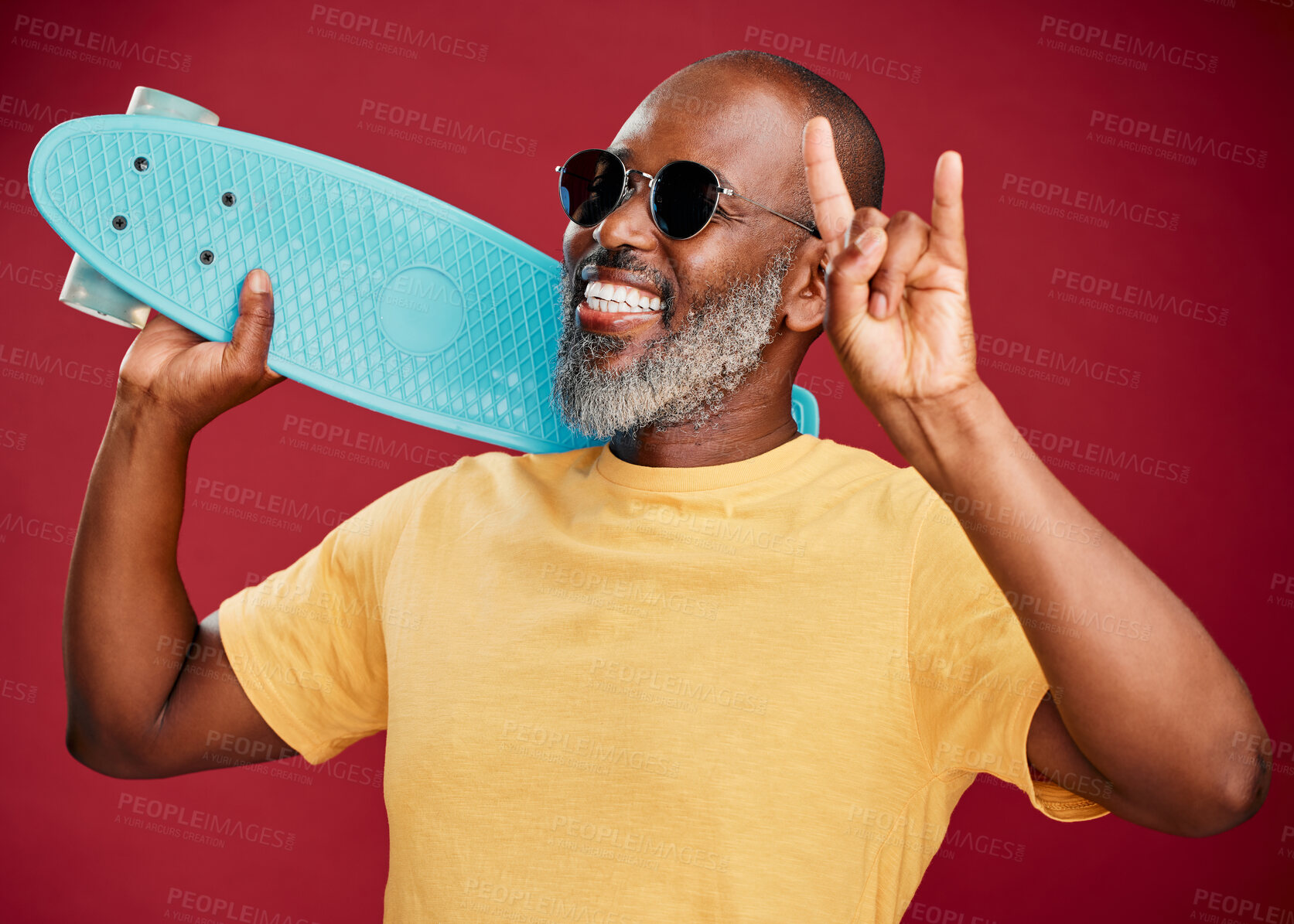 Buy stock photo One mature african american man standing with a mini skateboard in studio isolated against a red background. Handsome and carefree man wearing sunglasses and laughing happily. Summer means rock on