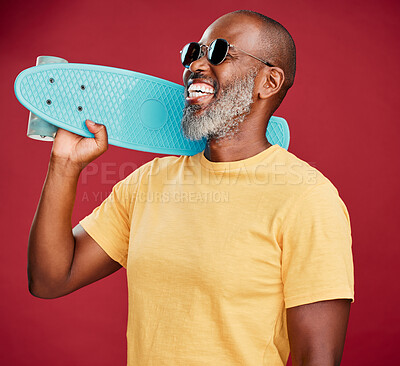 One mature african american man standing with a mini skateboard in studio isolated against a red background. Handsome and carefree man wearing sunglasses and laughing happily. He is ready for summer