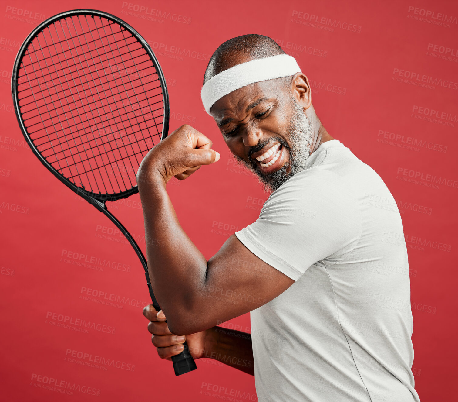 Buy stock photo One happy mature african american man standing against a red background in studio, flexing his bicep while posing with a tennis racquet. Smiling black man feeling fit and sporty while playing a match